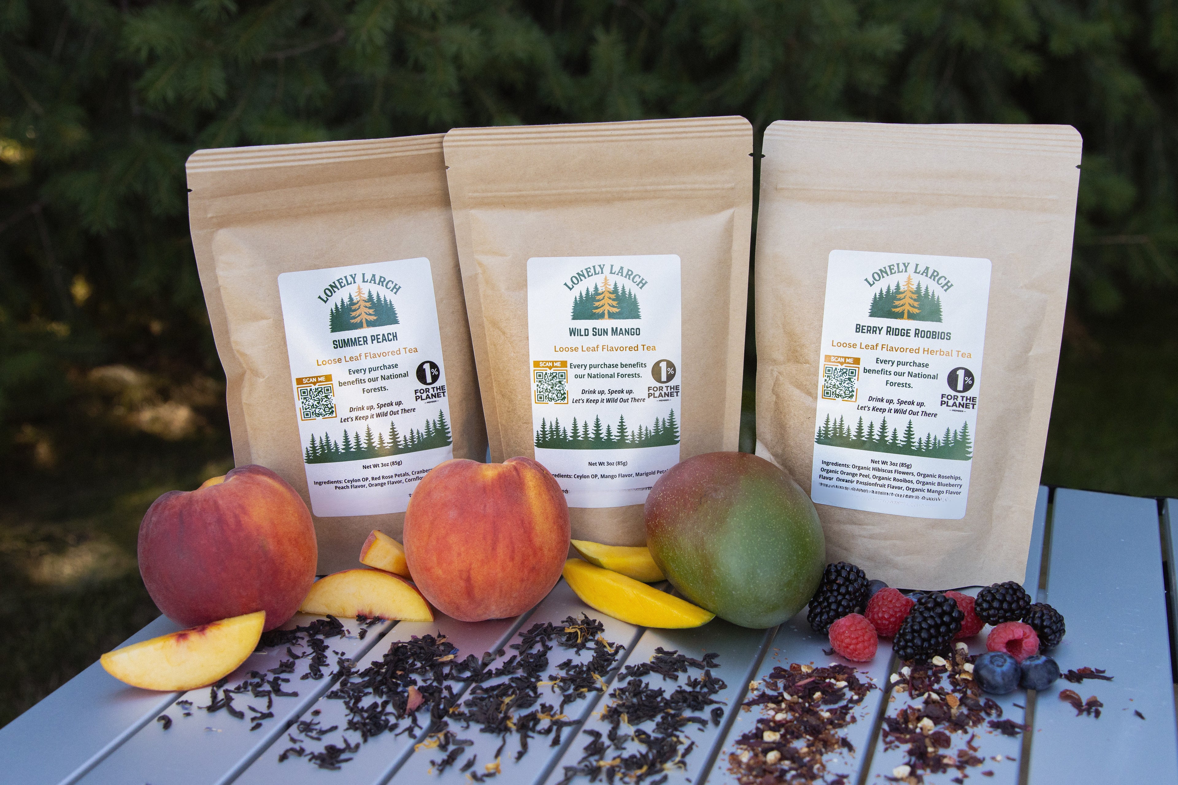 Three wooden tea bags with 'Lonely Larch' branding on a table with fruits and tea leaves.