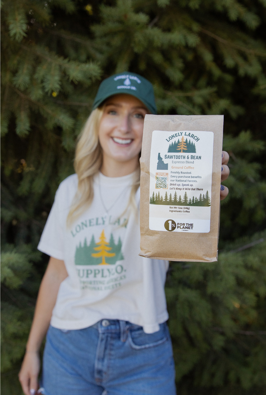 Person holding a package of 'Lonely Larch' coffee with trees in the background